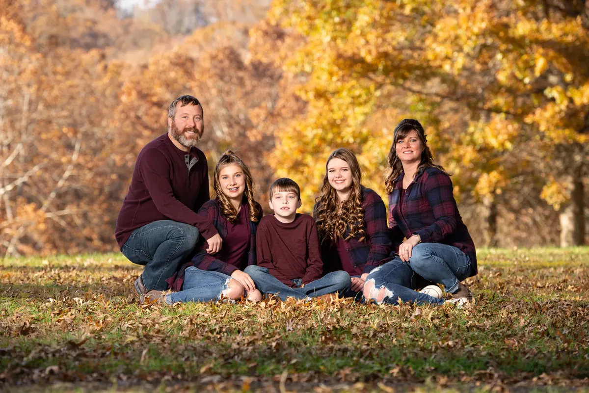 Family of five seated together beneath autumn trees