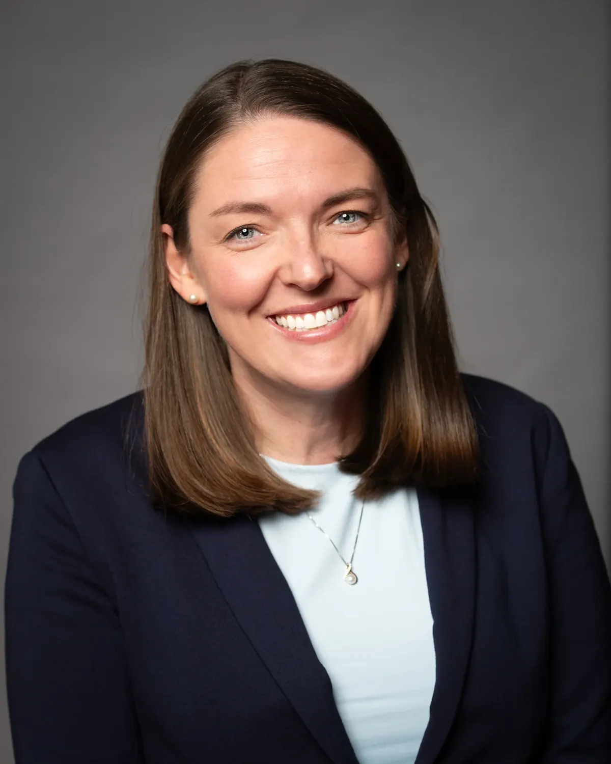 Woman in a navy blazer smiling against a gray background
