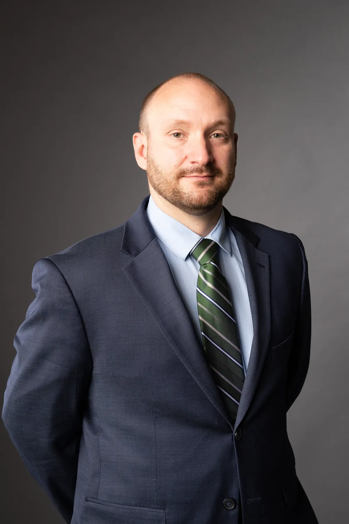 Man in a navy suit and green striped tie against a gray background
