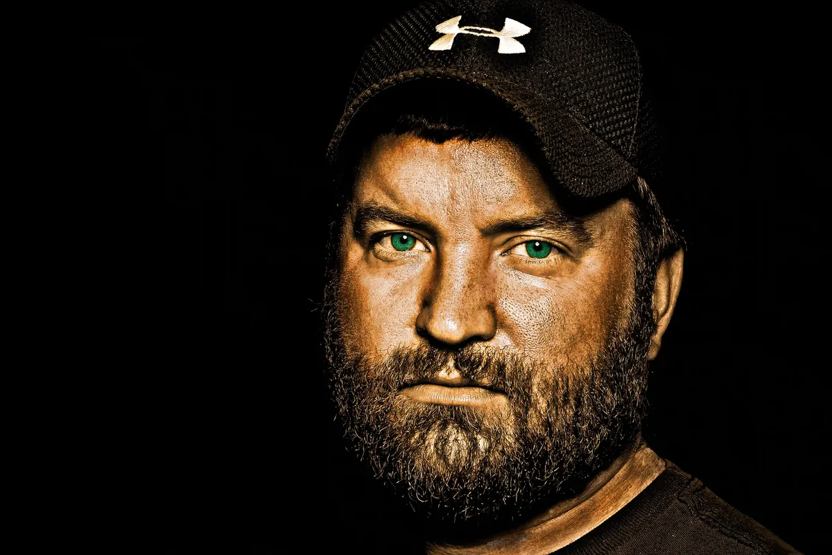 Dramatically lit close-up portrait of a bearded man wearing a black cap