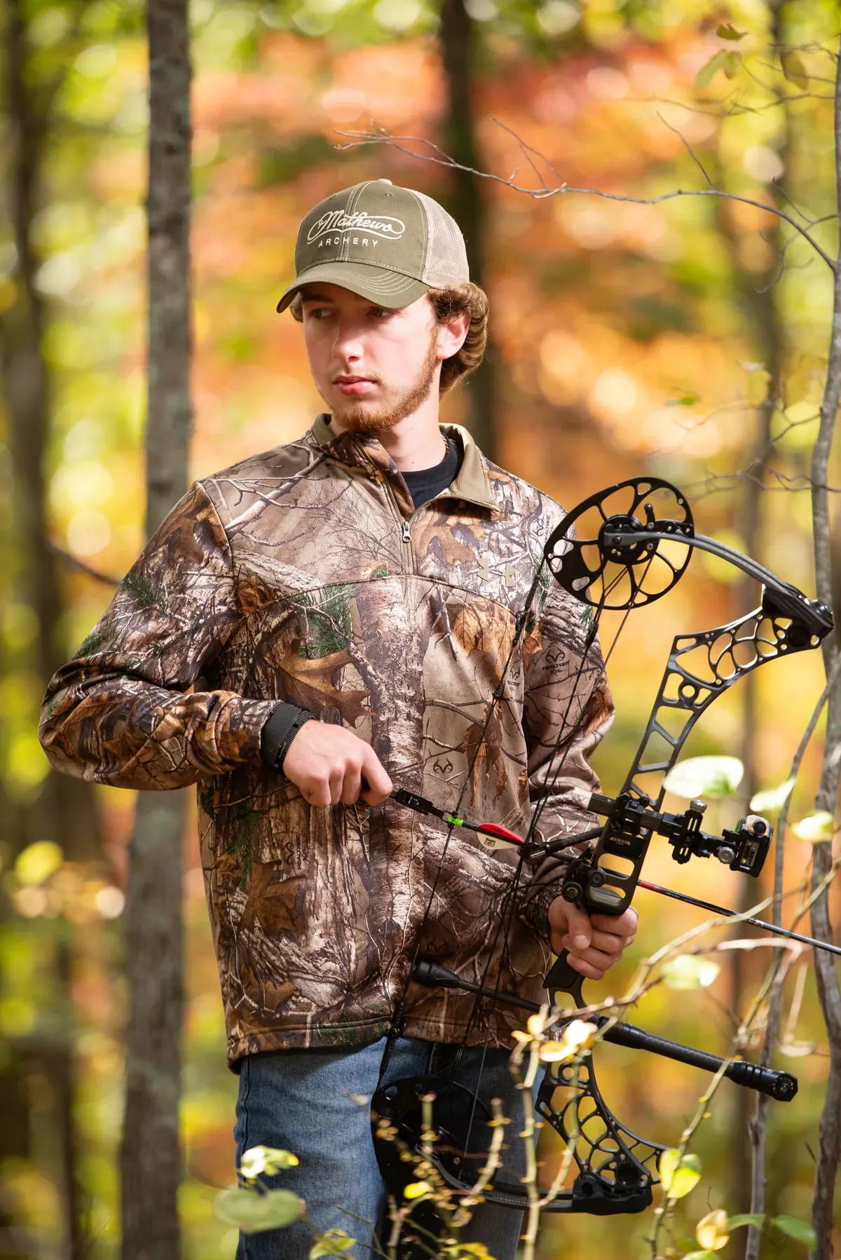 Senior in camouflage holding a compound bow in autumn woods