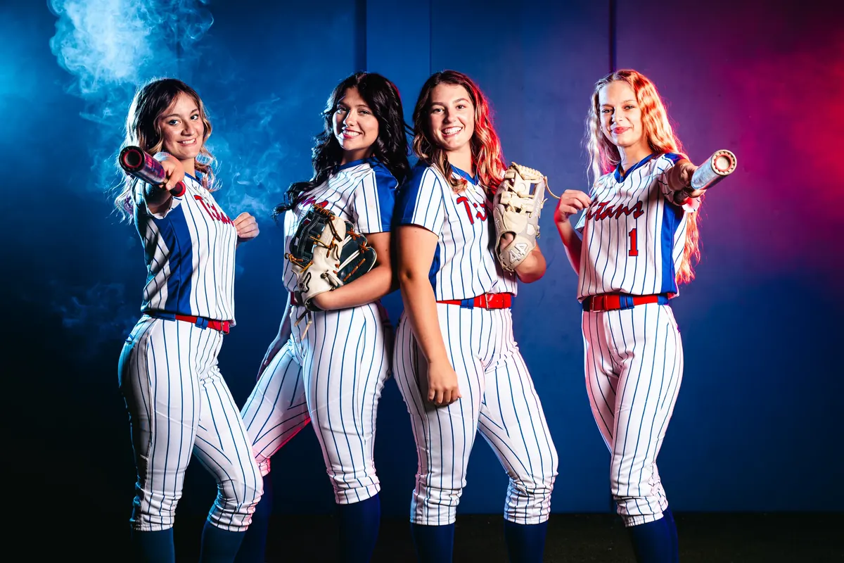 Four softball players with bats and gloves against blue and red lighting