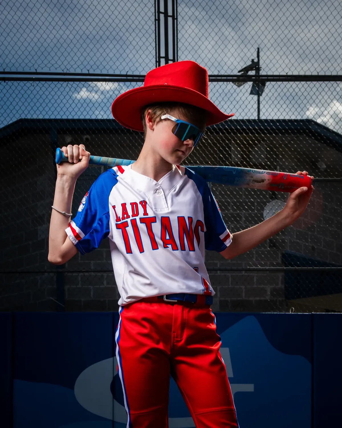 Softball player wearing a red hat with a bat across the shoulders